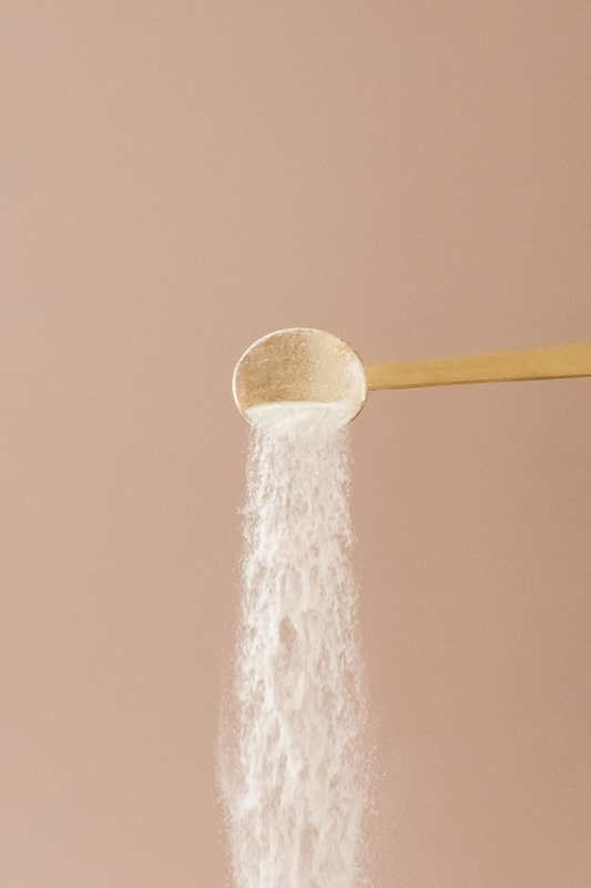 Wooden spoon pouring fine white powder against a soft pink background.