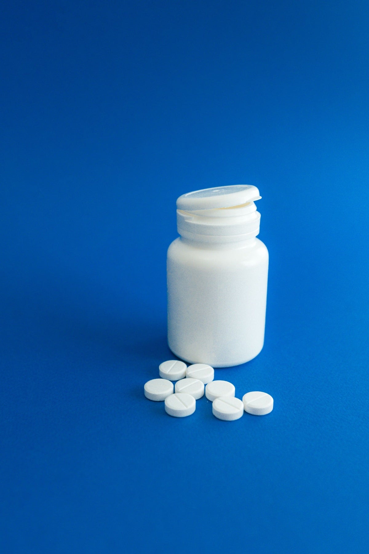 A plain white pill bottle and tablets on a blue surface.