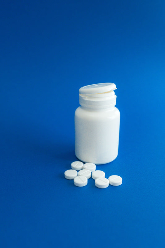 A plain white pill bottle and tablets on a blue surface.