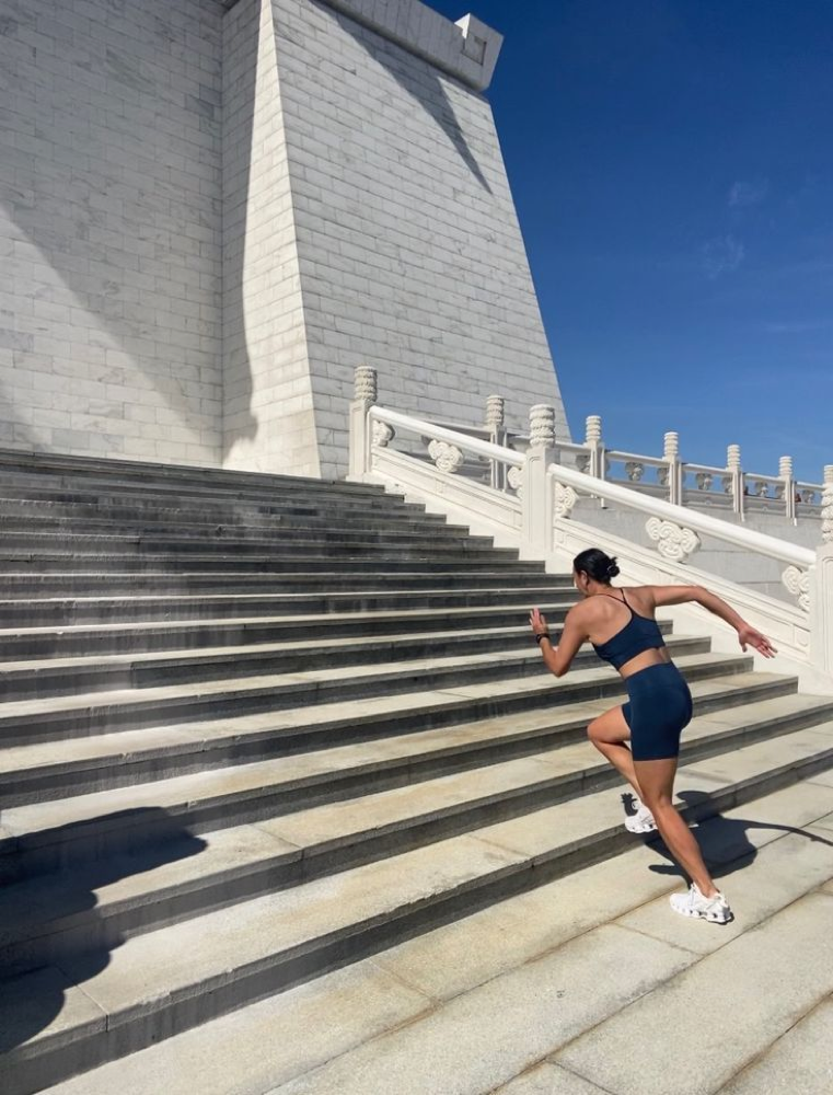 Woman sprinting up a broad outdoor stone staircase under a clear blue sky.